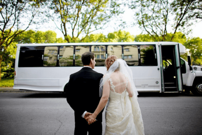 a bride and a groom in front of a white wedding bus